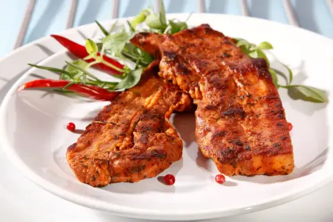 Dwa soczyste plastry boczek na grilla, przyprawione ziołami i podane z papryczkami chili.