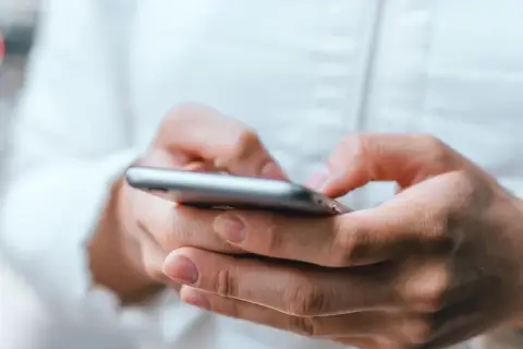 Dłonie trzymające smartfon, uważaj na oszustwa typu smishing, które mogą przyjść w każdej chwili.