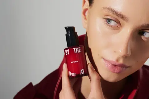 Kobieta z serum z peptydami w kosmetyce. Czerwona buteleczka z napisem "WAY TO GLOW" i "multipeptide face serum".