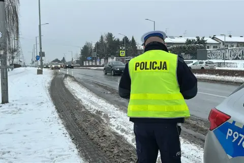 Policjant w kamizelce odblaskowej stoi przy drodze, gdzie kiedy zabierają prawko za prędkość. Śnieg i błoto na poboczu.