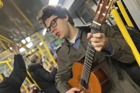 En ung man med glasögon spelar gitarr på tunnelbanan, en musikalisk själ med stockholm roots.