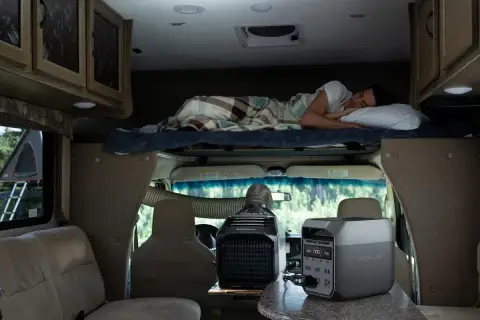 Un homme dort dans un camping-car 4 places. Une unité de climatisation portable et une station d'énergie sont visibles.