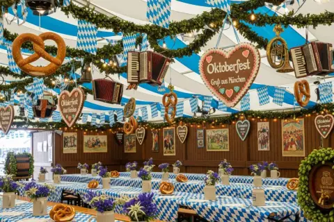 Wnętrze namiotu udekorowane na Oktoberfest. Wiszące precle, serca z napisem "Oktoberfest" i akordeony. Stoły przykryte niebiesko-białymi obrusami.