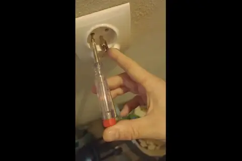 Próbnik świeci na bolcu gniazdka elektrycznego, sprawdzając napięcie.