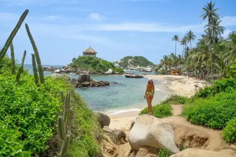 Mujer en bikini admira una playa paradisíaca con palmeras y un kiosko en una isla, ideal para un viaje a Colombia.