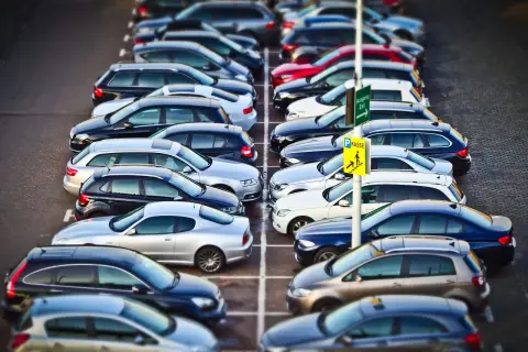 Rząd samochodów na parkingu. Znak "Kasse" sugeruje, że to parking płatny. KNF co to? To może być skrót od nazwy firmy zarządzającej parkingiem.