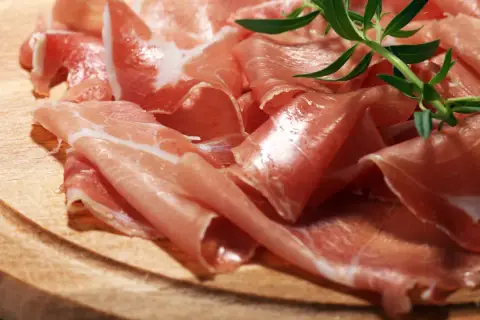 Cienkie plastry prosciutto crudo, ułożone na drewnianej desce, z gałązką rozmarynu. Pyszne, prawda?