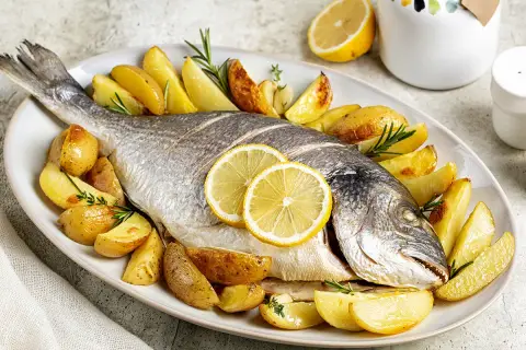 Dorade au barbecue à la portugaise, entière, dorée et savoureuse, accompagnée de pommes de terre rôties et de rondelles de citron.