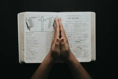Dłonie złożone w modlitwie nad otwartą Biblią, w której widnieje porównanie Starego i Nowego Testamentu. To chwila refleksji i psalmy uwielbienia.