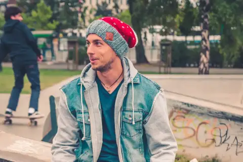 Chłopak w fajnej czapce dla chłopców i jeansowej kurtce siedzi na skateparku.