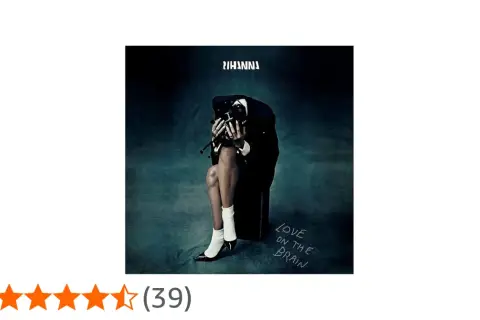 Rihanna w czarnym garniturze, siedząca z głową opuszczoną na dłonie, na tle mrocznego gradientu.