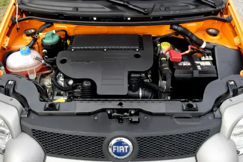 Silnik 1.3 Multijet w samochodzie Fiat. Widoczny akumulator, zbiornik płynu chłodniczego i osłona silnika.