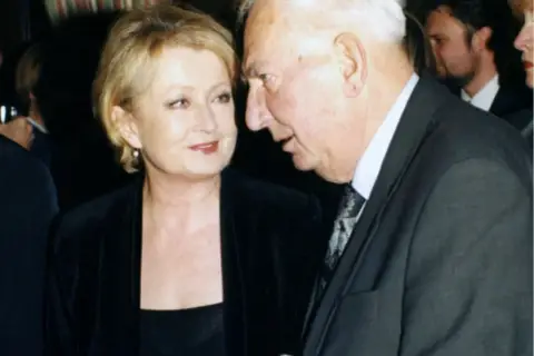 Magdalena Holoubek, córka Gustawa, rozmawia z mężczyzną w garniturze.