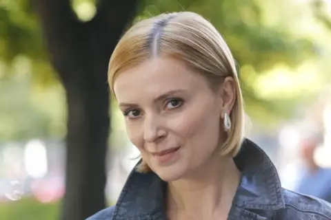 Portret Haliny Młynkowej z krótkimi blond włosami, w kurtce, na tle drzew.
