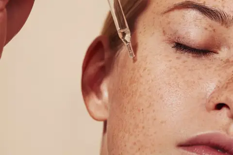 Kropla serum z pipety spada na piegowatą skórę. Dowiedz się, retinol co to i jak działa.