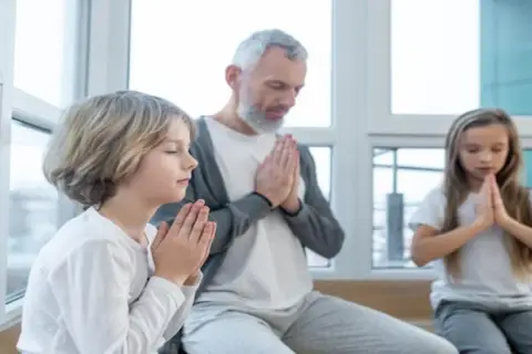 Dziadek z wnukami w ciszy składają dłonie do modlitwy o zdrowie dla rodziny.
