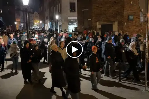 Tłum ludzi idzie ulicą nocą, trzymając świece. To wygląda jak Droga Krzyżowa.