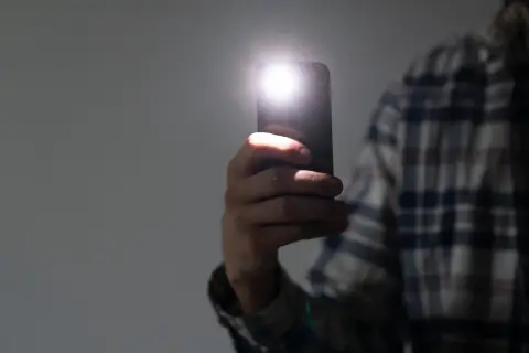 Dłoń trzyma telefon, którego latarka w telefonie rozświetla ciemność.