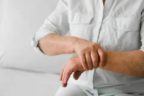 Osoba w białej koszuli masuje nadgarstek, odczuwając ból stawów.