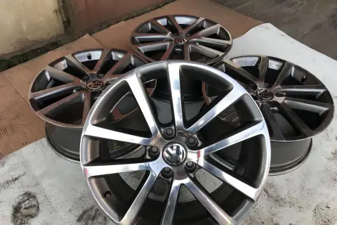 Cztery aluminiowe felgi Volkswagen z logo, ułożone na ziemi.