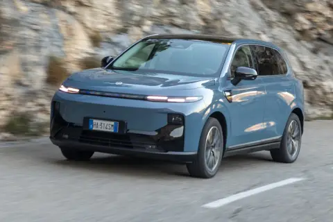 Niebieski Leapmotor B10 przemierza krętą drogę wśród skalistych zboczy.