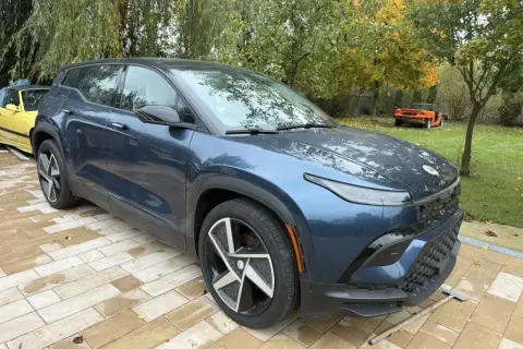 Nowy, granatowy Fisker SUV stoi na wybrukowanym podjeździe. W tle żółty i pomarańczowy samochód.