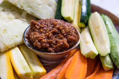 A bowl of savory miso dip is surrounded by fresh, colorful crudités: sliced zucchini, yellow squash, carrots, and cabbage wedges, ready for dipping.