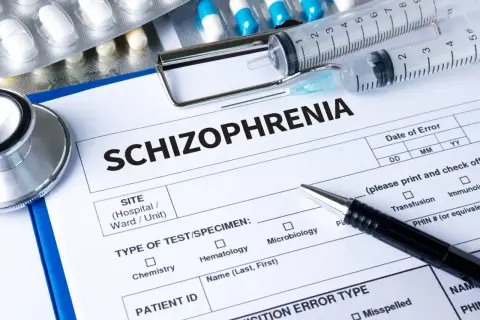 Lekarz wypełnia dokumentację medyczną dotyczącą schizofrenii, obok leków, w tym risperidon, strzykawek i stetoskopu.