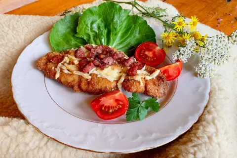 Schab po góralsku, panierowany kotlet z serem i boczkiem, podany z pomidorami i sałatą.