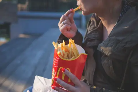 Kobieta je frytki z czerwonego opakowania McDonald's.