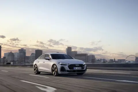 Białe audi hybryda jedzie po autostradzie z widokiem na miasto o zachodzie słońca.