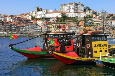 Porto na weekend: tradycyjne łodzie Rabelo na rzece Douro, z kolorowymi domami i zabytkowymi budynkami w tle.