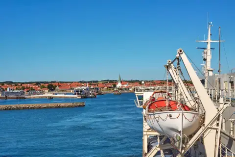 Widok na port z promem, łodzią ratunkową i miastem w tle.
