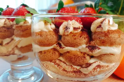 Pyszne tiramisu w pucharkach, przełożone kremem i biszkoptami, ozdobione truskawkami i kakao.