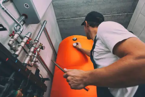 Technik sprawdza temperaturę na dużym, pomarańczowym bojlerze w kotłowni z piecem gazowym.