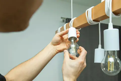 Ręce wkręcają żarówkę LED do drewnianego elementu lampy. Czy ledy się nagrzewają? Ta żarówka wygląda na chłodną.