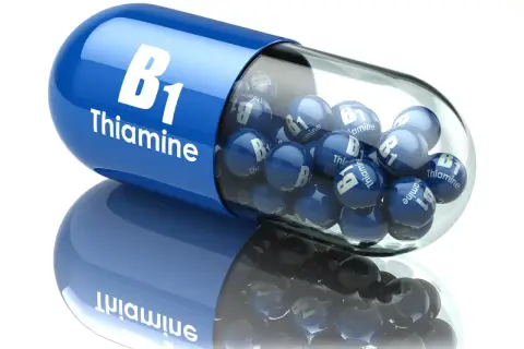 Niebieska kapsułka z napisem "B1 Thiamine" wypełniona małymi kulkami z tym samym oznaczeniem. Tiamina w pigułce.