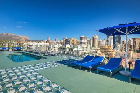 Terraza con piscina y tumbonas azules en Barceló Benidorm, con vistas a la ciudad y montañas.