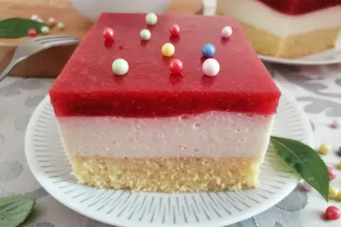Pyszna żelka truskawkowa z mrożonych truskawek, z kremową warstwą i biszkoptem, ozdobiona kolorowymi kuleczkami.