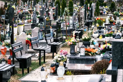 Ławki na cmentarzu, przygotowane na wizytę bliskich. Wiele zniczy i kwiatów świadczy o pamięci.