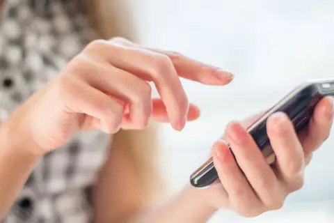 Dłonie obsługują smartfon, palce przesuwają się po ekranie, jakby wybierały opcję z menu +20 kierunkowego.