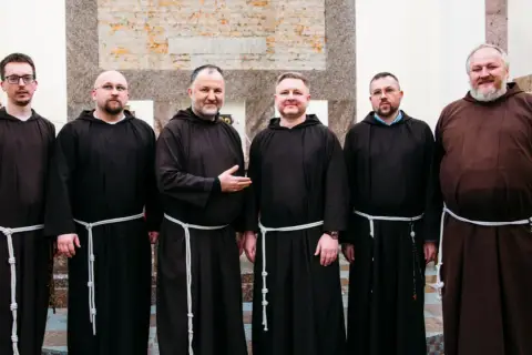 Sześciu mężczyzn w brązowych habitach, każdy z białym sznurem przepasanym w pasie. To grupa kapucynów.