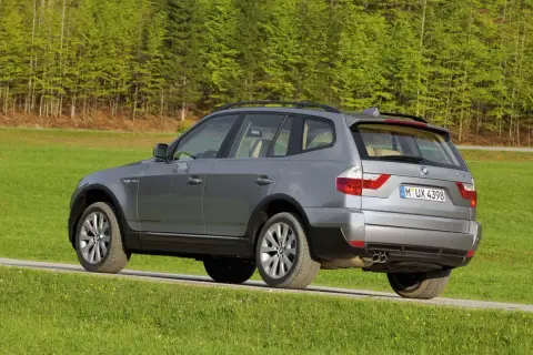 Szary BMW E83 na tle zielonego lasu i łąki.