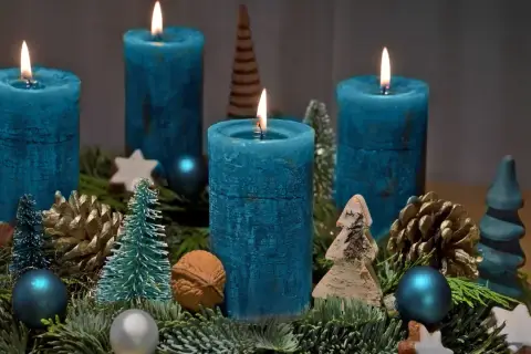 Ein selbstgebastelter Adventskranz mit vier blauen Kerzen, Tannenzweigen, Zapfen und kleinen Bäumchen.