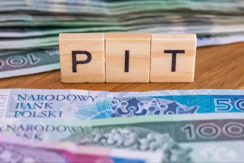 Drewniane klocki z literami "PIT" na tle polskich banknotów. To symbol ulgi na dzieci, która może pomóc w rozliczeniu podatkowym.