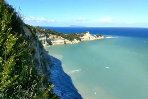 Widok z klifu podczas **Korfu trekking** na turkusowe morze i skaliste wybrzeże.