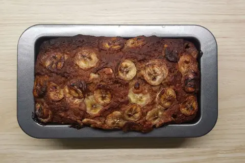 Upieczony proteinowy chlebek bananowy z plasterkami banana na wierzchu, w metalowej formie.