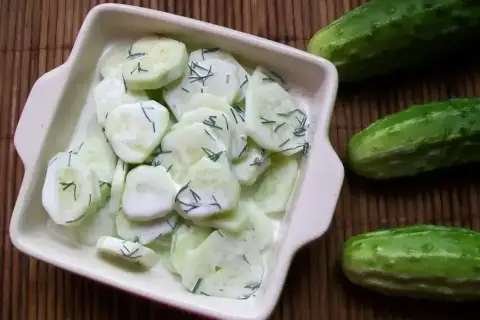 Mizeria na słodko z koperkiem w kremowym sosie, obok świeże ogórki. Idealna na letni obiad.