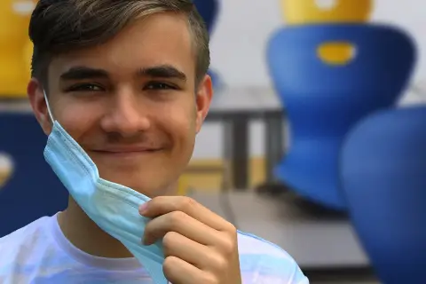 Joven sonriente se quita mascarilla, recordando la importancia de conocer los **covid en niños sintomas** para su bienestar.