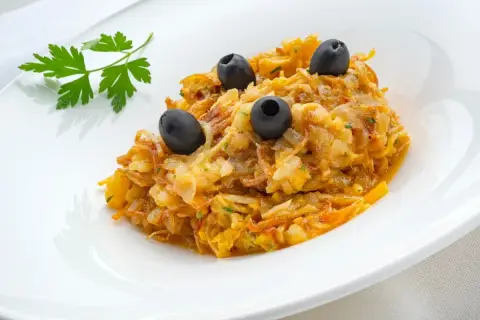Delicioso revuelto de bacalao con aceitunas negras y perejil fresco, servido en un plato blanco.